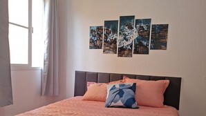 Une chambre à coucher avec un lit, une tête de lit, une fenêtre avec des rideaux et un mur orné de trois tableaux.