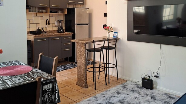 Une cuisine compacte dotée d’un réfrigérateur intégré, un coin repas avec une table et des chaises, et un téléviseur fixé au mur.