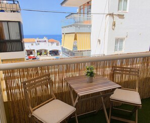 A balcony with two wooden chairs and a small table, overlooking a street with buildings and a clear blue sky. - Centrally located apartment, ideal for families and very close to Playa de las Vistas Beach. (Arona)