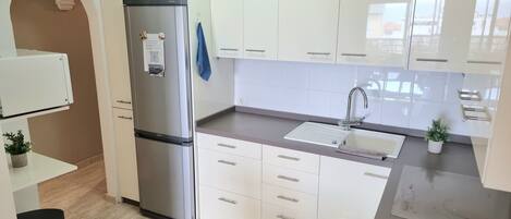 A modern kitchen with white cabinets, a stainless steel refrigerator, a sink, and a small potted plant.