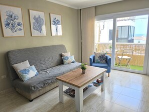 A living room with a grey sofa, a wooden coffee table, and a blue armchair. There are three framed artworks on the wall.