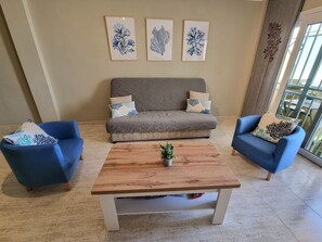 A living room with a grey sofa, two blue armchairs, a wooden coffee table, and three framed coral reef artworks on the wall.