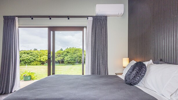 Habitación de hotel con una cama grande, una mesita de noche con lámpara y vistas a un jardín a través de una puerta corredera.