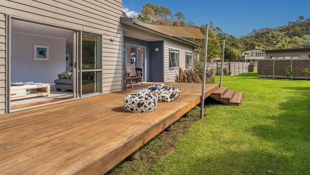 A modern house with a wooden deck, sliding glass doors, and a grassy backyard. - Flaxmill Haven - Cooks Beach Holiday Home (Whitianga)