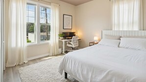 Un dormitorio con una cama, un escritorio con computadora, una silla y una ventana con cortinas.