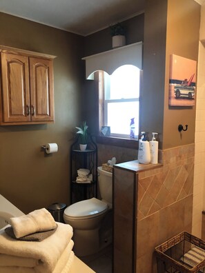A bathroom with a toilet, a sink with toiletries, a towel rack, and a window.