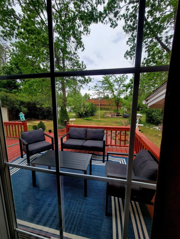 A deck with outdoor furniture, a blue rug, and a view of a garden and house.