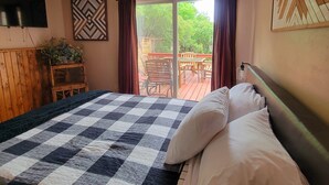 Een slaapkamer met een geruit beddegoed, een aan de muur bevestigde televisie, een decoratieve wand en een uitzicht op een terras met meubilair.