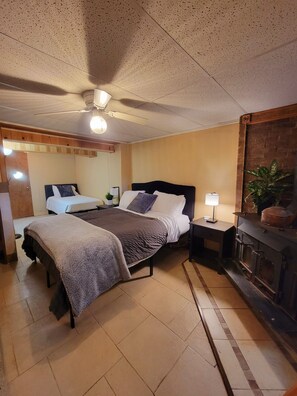 A bedroom with a bed, bedside tables, a ceiling fan, a lamp, and a fireplace.