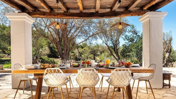 An outdoor dining area with a wooden pergola, stone flooring, and wicker chairs. - New! Villa Can Cardona (Santa Agnès de Corona)