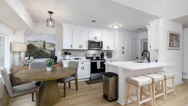 A modern kitchen with white cabinetry, a central island with stools, and a dining area with a round table and chairs. - Clean & Comfortble Poker House Near Kalahari! (Round Rock)