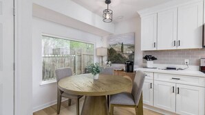 A modern kitchen with white cabinets, a round wooden table, and a view of the outdoors through a large window. - Clean & Comfortble Poker House Near Kalahari! (Round Rock)