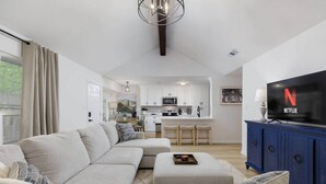 A modern living room with a sofa, ottoman, and a flat-screen TV displaying the Netflix logo. - Clean & Comfortble Poker House Near Kalahari! (Round Rock)