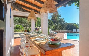 An outdoor dining area with a pool, white plastic chairs, and a wooden table set for a meal. - New! Villa Can Guillem Patri (Ibiza)