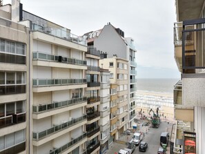 A multi-story building with balconies, a view of the sea, and a busy street with vehicles.
