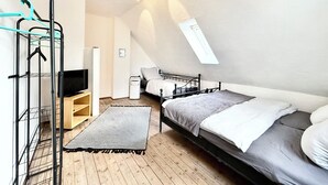 Un dormitorio pequeño y moderno con una cama elevada, televisor, escritorio y ventana.