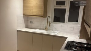 Cuina amb un rentaplat amb encastrat, armaris de fusta, una finestra i una cuina a gas.