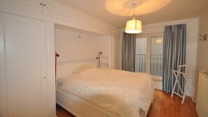 Ein Schlafzimmer mit Bett, einer Hängelampe, einem Fenster mit Vorhängen und einer Heizung.