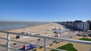 Blick vom Balkon auf einen Sandstrand, eine Promenade und eine Reihe von Gebäuden.