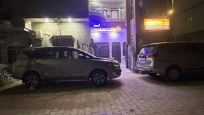 Een gebouw met een bord waarop 'DWARAKI PALACE' staat, met de aanduiding voor kamers met en zonder airconditioning. Er staan twee auto's geparkeerd voor, en de ingang heeft een trap.