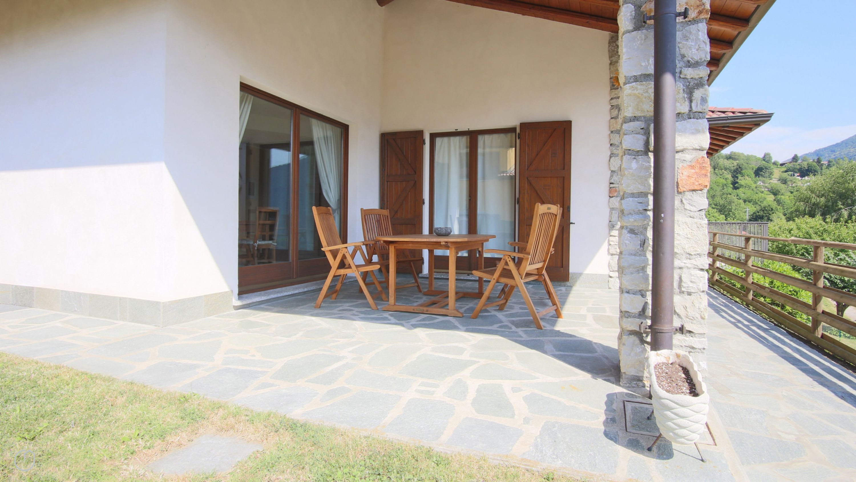 A patio with a table and chairs, stone flooring, and a view of greenery and hills.