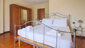 Un letto rifatto con lenzuola e asciugamani bianchi, un armadio in legno, uno specchio a figura intera e un comodino con una lampada.