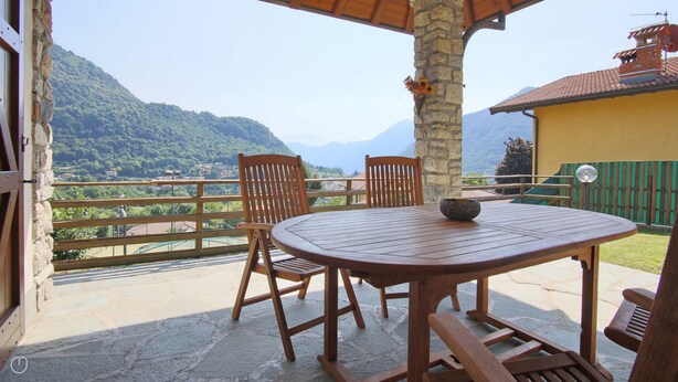 Un tavolo e sedie di legno su un balcone con pavimento in pietra, con vista su un paesaggio montuoso.