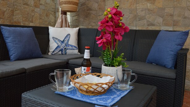 A wicker sofa with blue cushions, a wicker basket, and a bottle of beer on a table with two glasses.