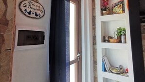 A room with a stone wall, a welcome sign, a door with a black curtain, and a shelf with various items.