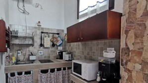 A compact kitchen with a stone accent wall, a microwave, a coffee maker, and a small window.