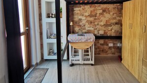 A room with a bunk bed, a wooden cabinet, a small table with a patterned tablecloth, and a stone wall.