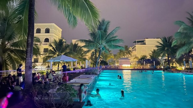 A pool area with palm trees, lounge chairs, and a building in the background. - Kaira Boutique Hotel (Duong To)