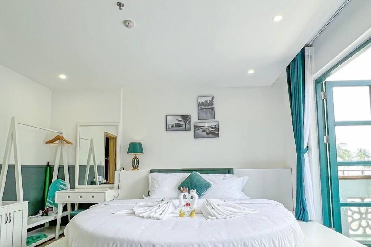 Une chambre d’hôtel avec un grand lit, une commode, un miroir, une lampe et une fenêtre avec des rideaux.