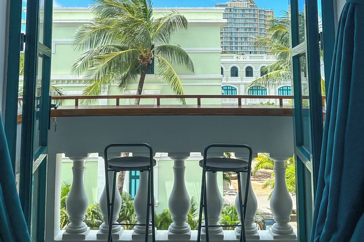 Un balcon avec vue sur un palmier et des immeubles.