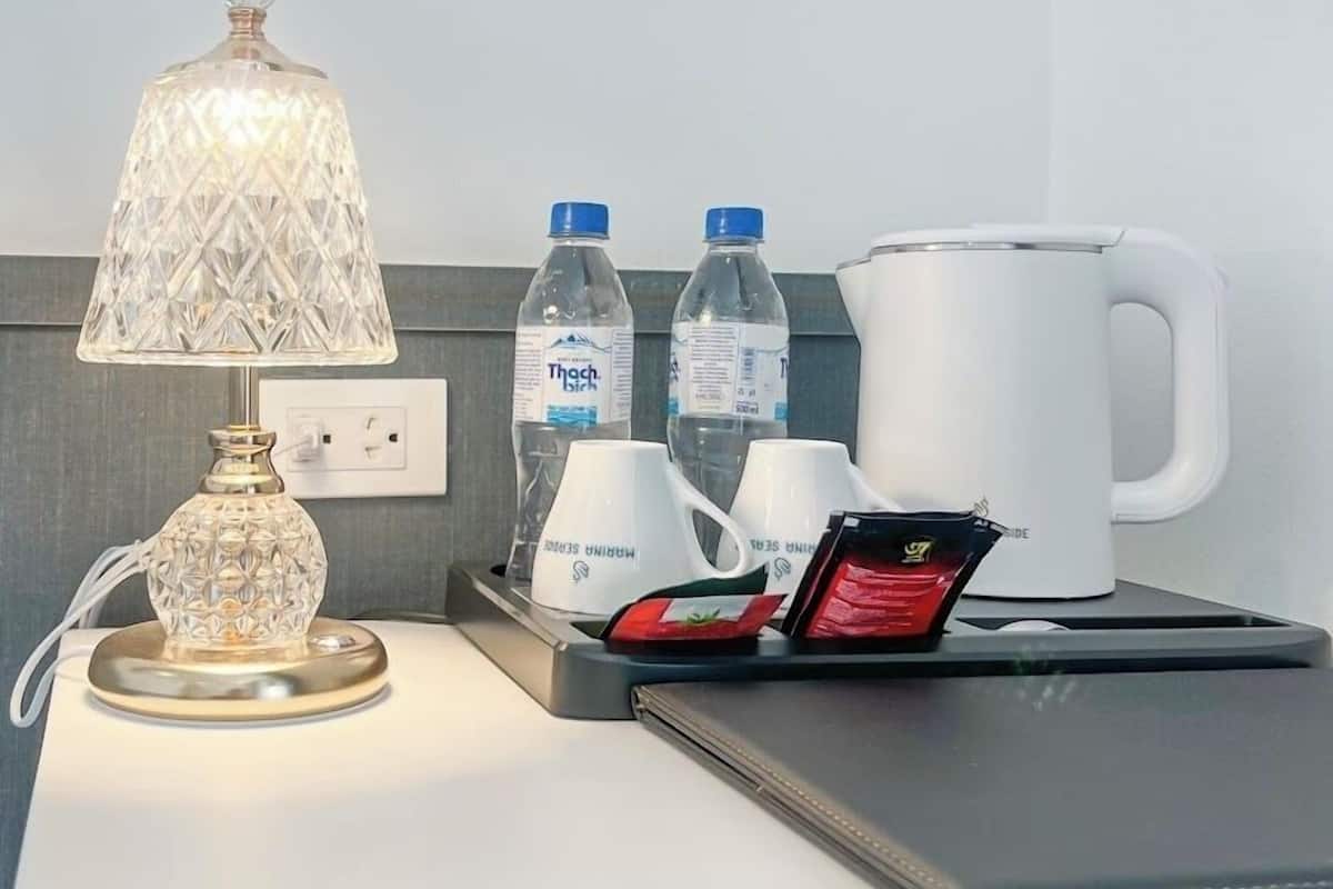 Une chambre d’hôtel équipée d’une lampe de chevet, de bouteilles d’eau, d’une machine à café et d’un téléphone portable posé sur un support de recharge.