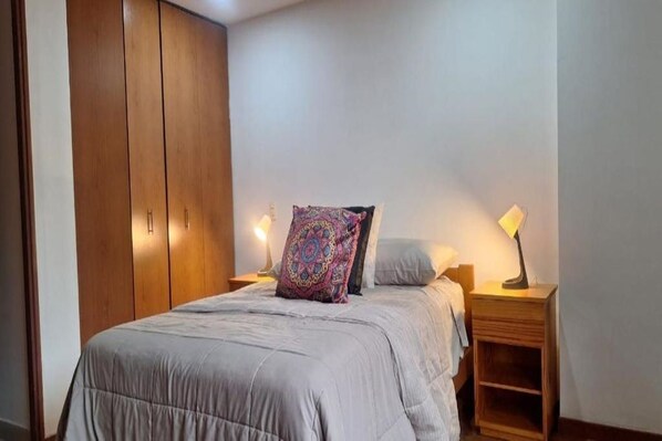 A bedroom with a bed, two bedside tables, a wardrobe, and a patterned pillow.