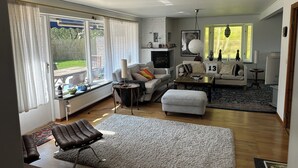 A modern living room with a fireplace, a sofa set, a coffee table, and a view of the garden through large windows. - Big house in a secluded area in beautiful Skanör (Skåne län)