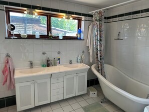 A bathroom with a white sink, vanity, and bathtub. There is a window above the sink, and a shower curtain with a floral pattern. - Big house in a secluded area in beautiful Skanör (Skåne län)
