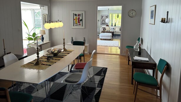 A dining area with a long table, chairs, and a chandelier. There is a view into another room with a sofa and a clock on the wall. - Big house in a secluded area in beautiful Skanör (Skåne län)