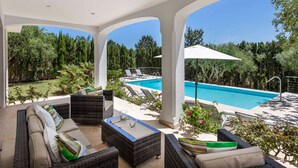 A covered outdoor area with a pool, wicker furniture, and a view of the surrounding greenery. - Villa Bella Vista in Sa Pobla (Sa Pobla)