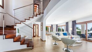 Un amplio espacio de estar con una escalera moderna, un conjunto de sofás blancos y una zona de comedor.