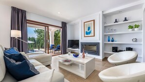 Una sala de estar moderna con sofá, mesa de centro y televisor. Cuenta con chimenea, balcón con vistas y estantería decorativa.