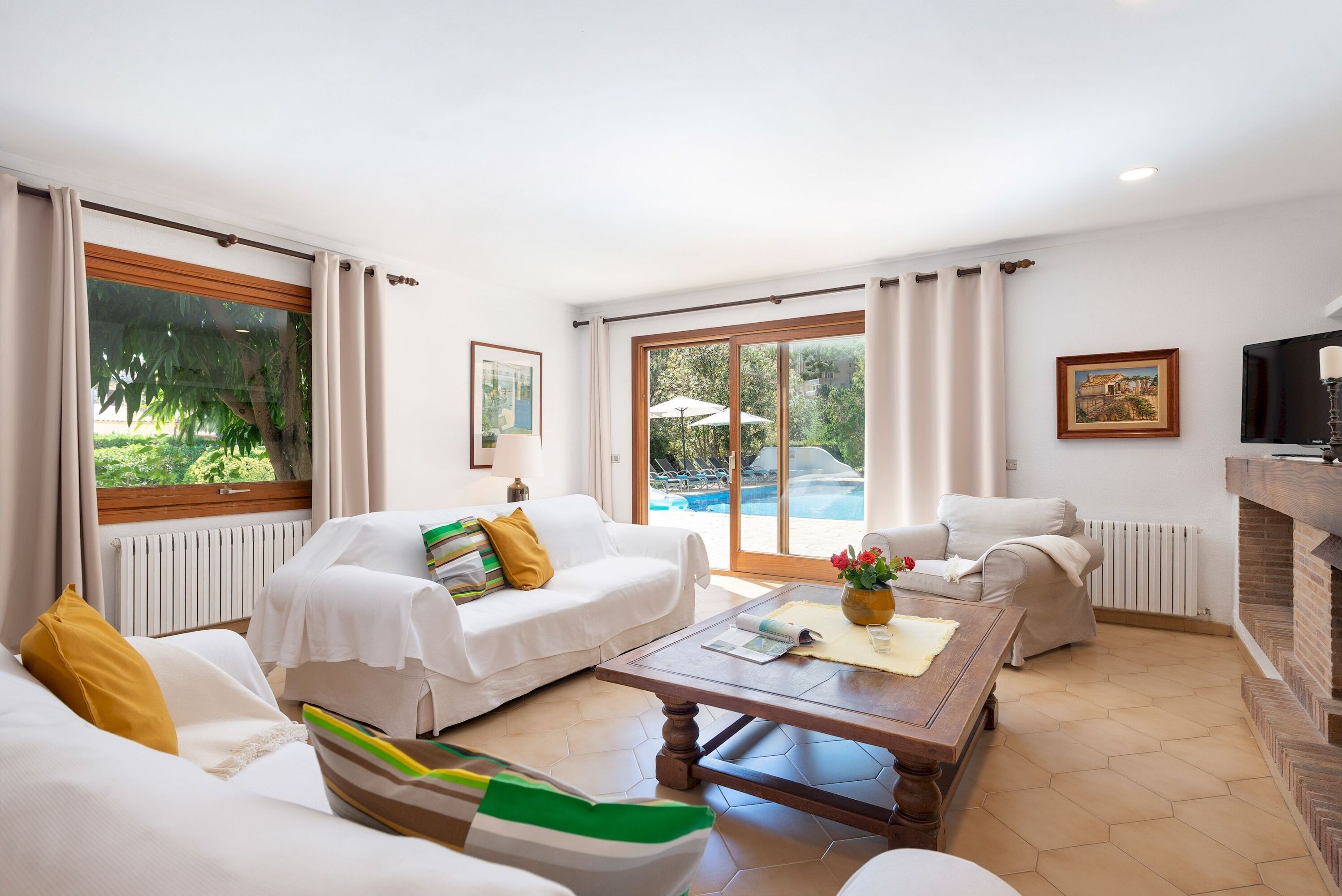A spacious living room with a large window, a fireplace, and a view of an outdoor pool.