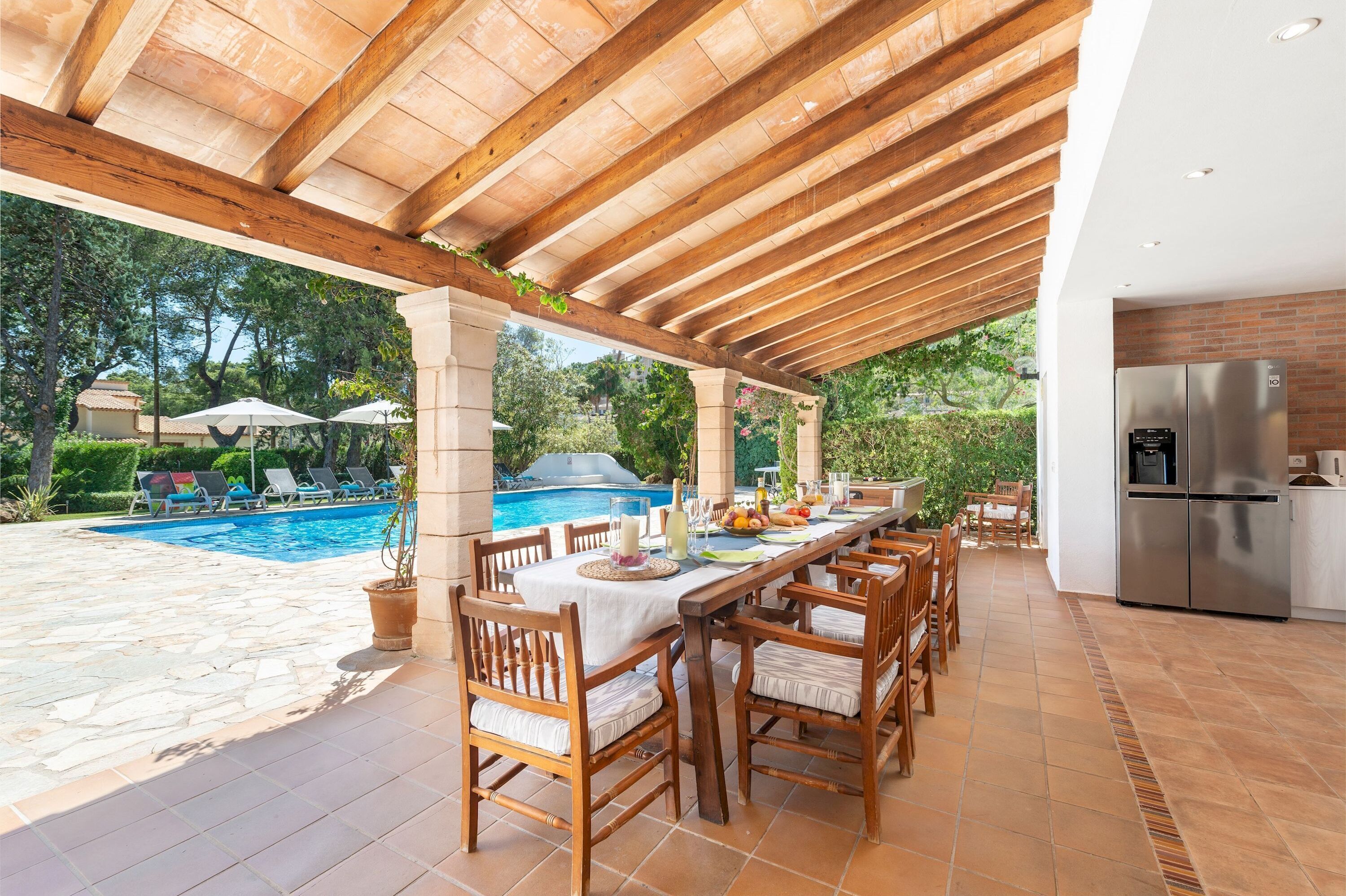 An outdoor patio with a pool, wooden furniture, and a kitchen area.