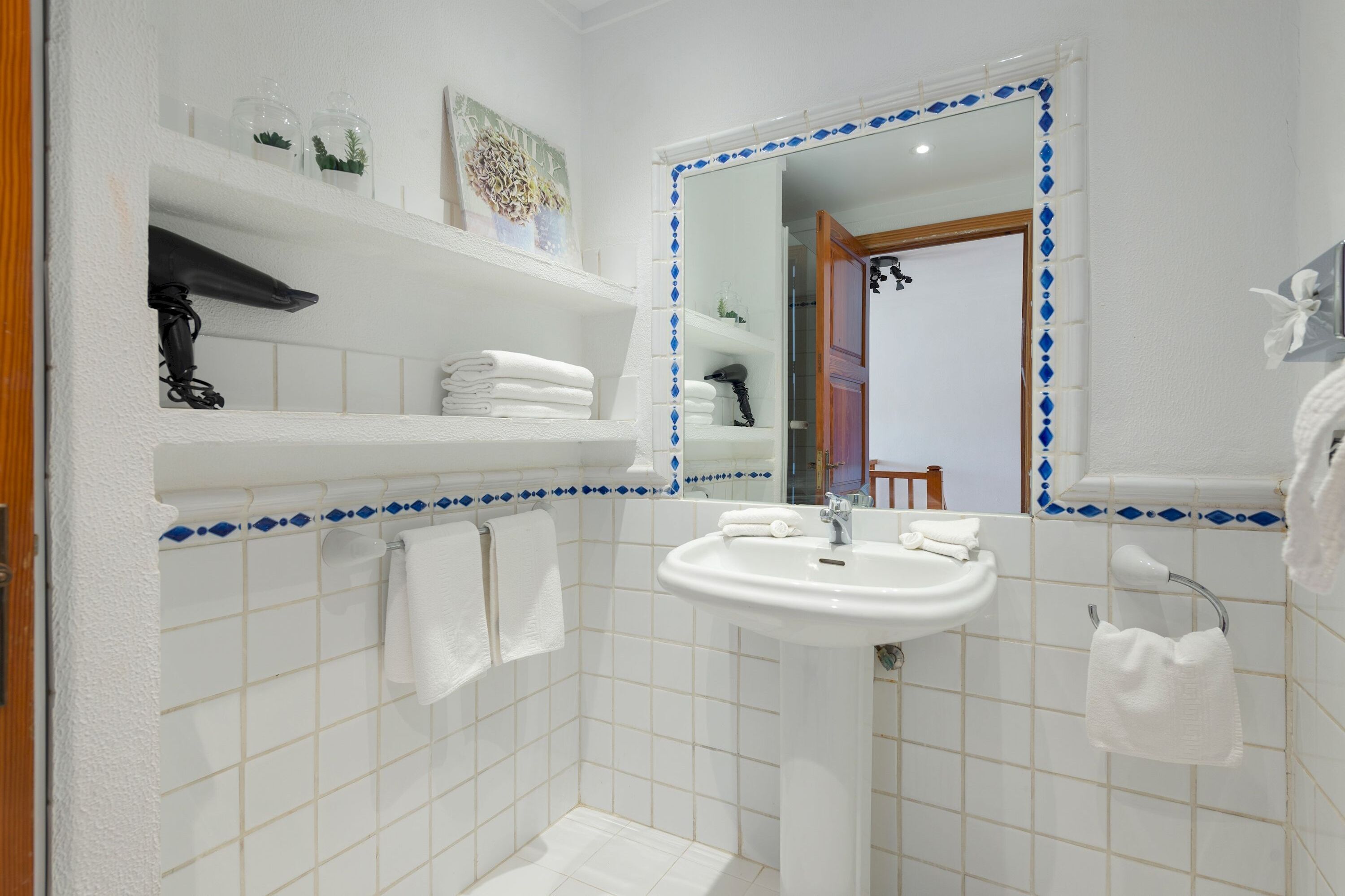 A bathroom with a white sink, a mirror with a blue diamond border, and shelves with towels and toiletries.