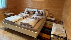 Una cama doble con dos mesitas de noche, una mesilla, una lámpara, una silla y un cuadro en la pared.