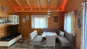 Un interior acogedor de cabaña con techo de madera, un sofá, una mesa de comedor y un televisor.