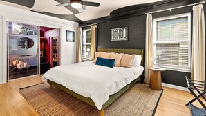 Un dormitorio moderno con una cama, un ventilador de techo, una ventana con cortinas y un televisor montado en la pared.