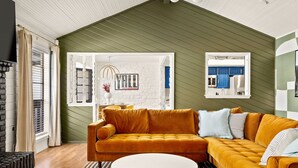 Una sala de estar moderna con un sofá grande color naranja, una mesa de centro blanca y una pared verde con detalles de ladrillo blanco.