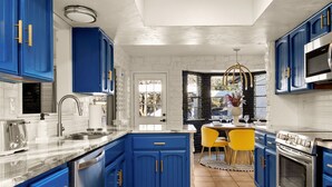 Una cocina moderna con armarios azules, electrodomésticos de acero inoxidable y una zona de comedor con sillas amarillas.